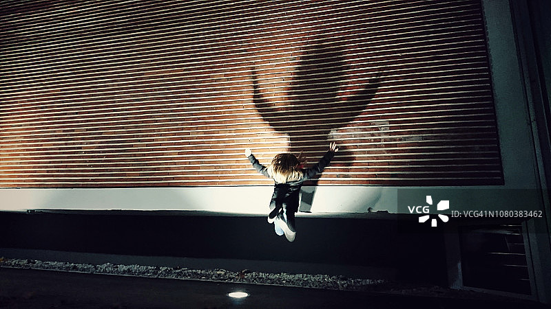 夜晚，女孩跳跃的身影在砖墙上投下长长的影子图片素材