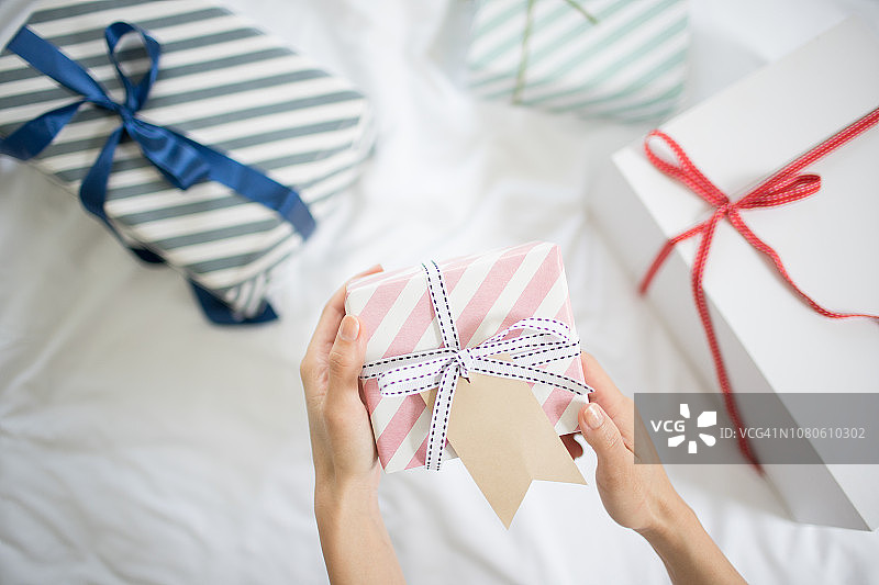 女人手在床上拿着带礼品标签的礼品盒图片素材