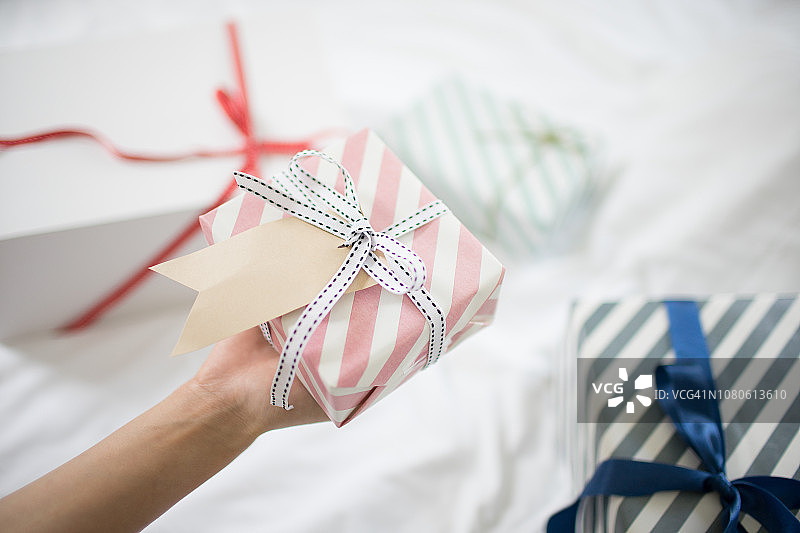 女人手在床上拿着带礼品标签的礼品盒图片素材