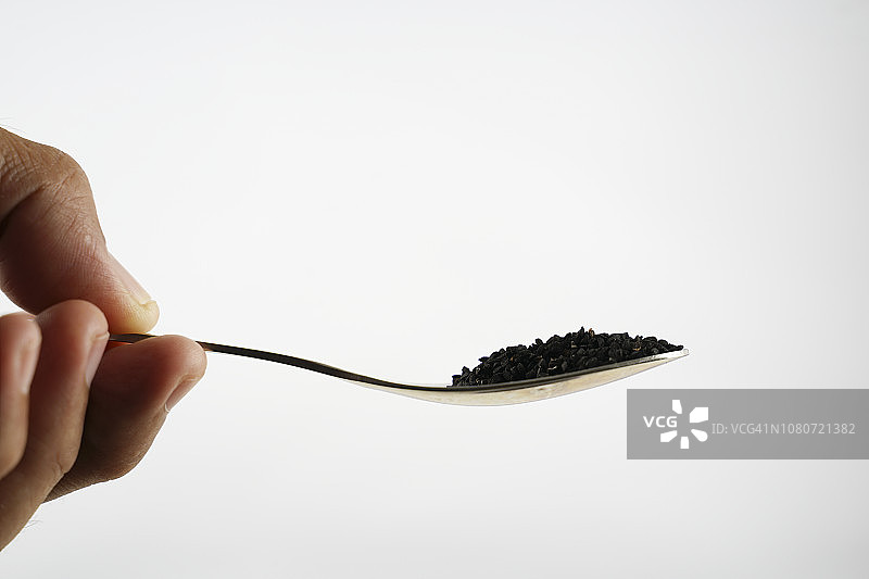 不锈钢勺子里的黑色香菜籽与白色背景图片素材