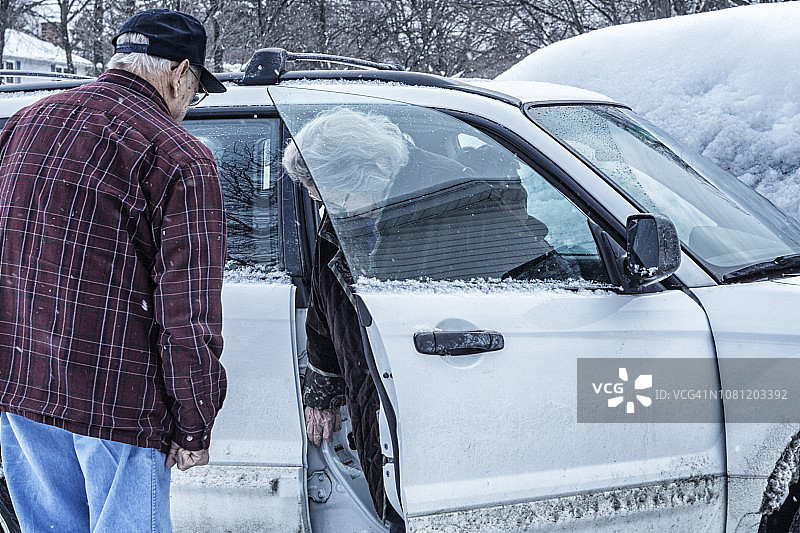 老年夫妇进入冬季暴风雪中的汽车图片素材