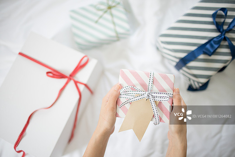 女人手在床上拿着带礼品标签的礼品盒图片素材
