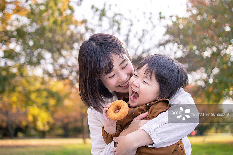 年轻的母亲和儿子在公园里愉快地吃甜甜圈图片素材