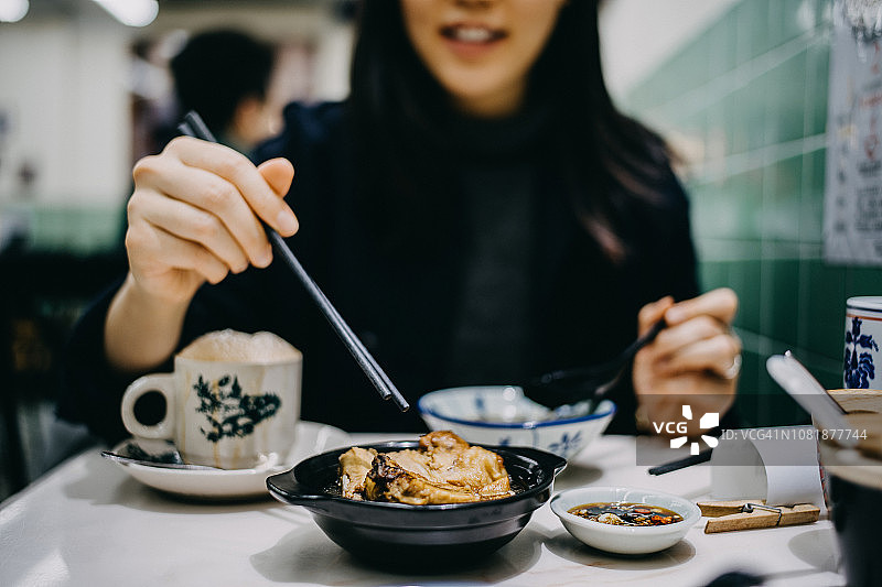 快乐的年轻女人在传统餐厅享用肉骨茶和拉茶图片素材