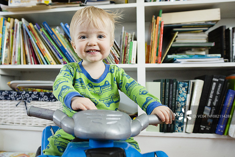 男婴骑玩具摩托车，背景为家中书架图片素材