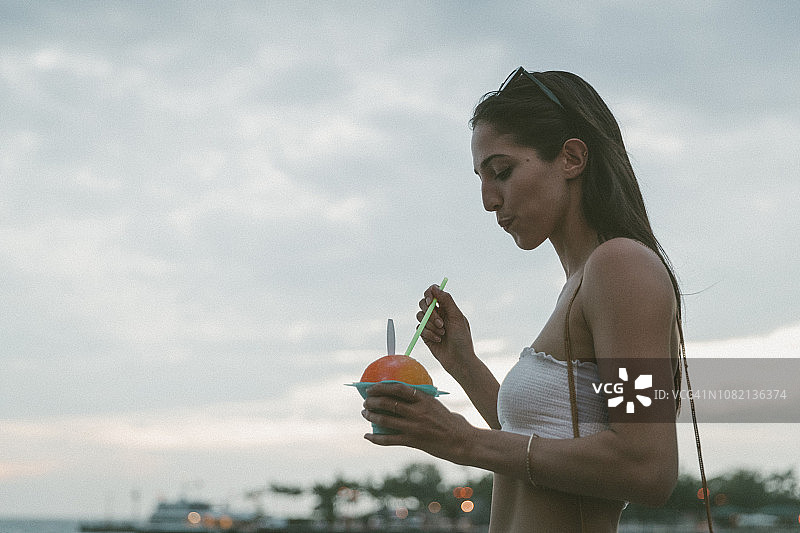 侧面的女人吃沙漠，而反对多云的天空图片素材