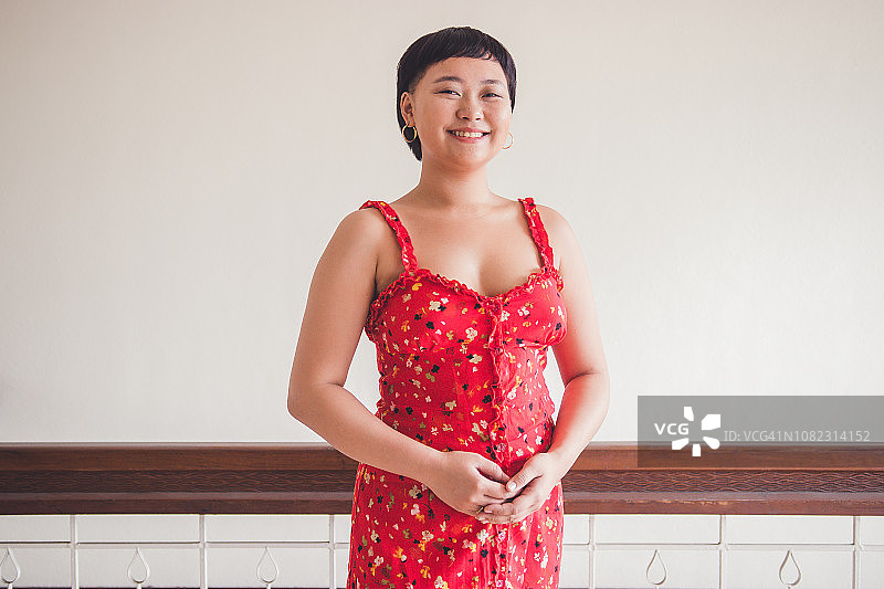 年轻女子站在墙前，双手交叉，对着镜头微笑图片素材