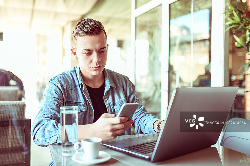 在酒吧喝咖啡时使用便携设备的年轻男人图片素材