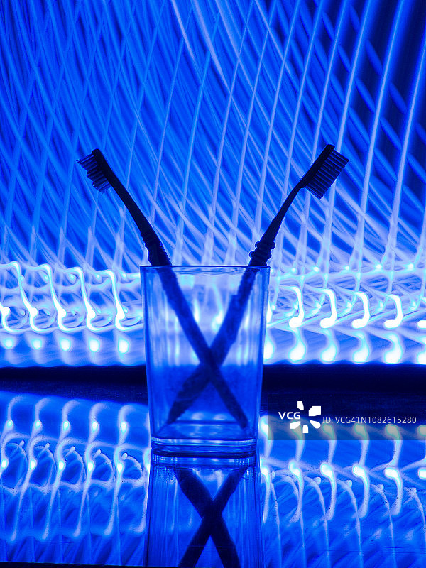 反光表面透明玻璃杯中的两把刷子，蓝白线条背景，清洁环境、实验室，蓝色线条灯光背景，光绘，概念自然图片素材