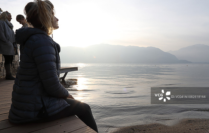 年轻女人在湖上码头放松，家人在身后图片素材