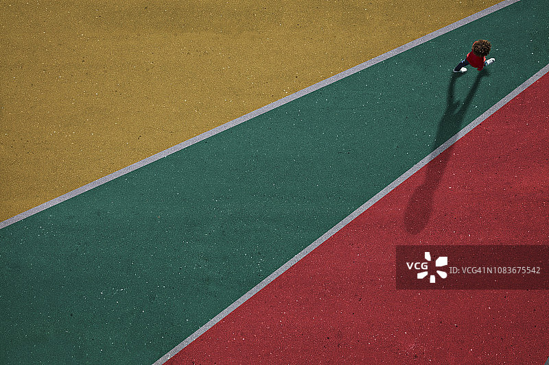 穿着红色衣服的孩子走过红、绿、蓝相间的沥青路面图片素材