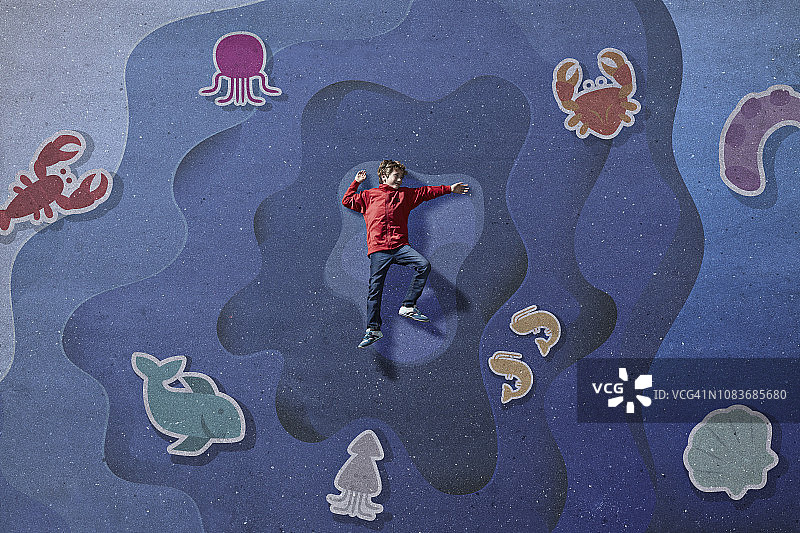 男孩躺在画出的海洋背景中，周围是海洋生物图片素材