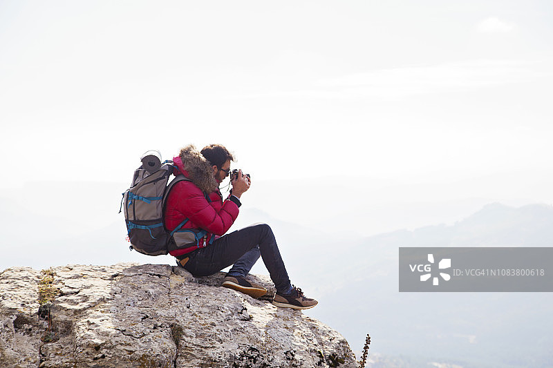 年轻旅行者坐在山上拍摄日落图片素材