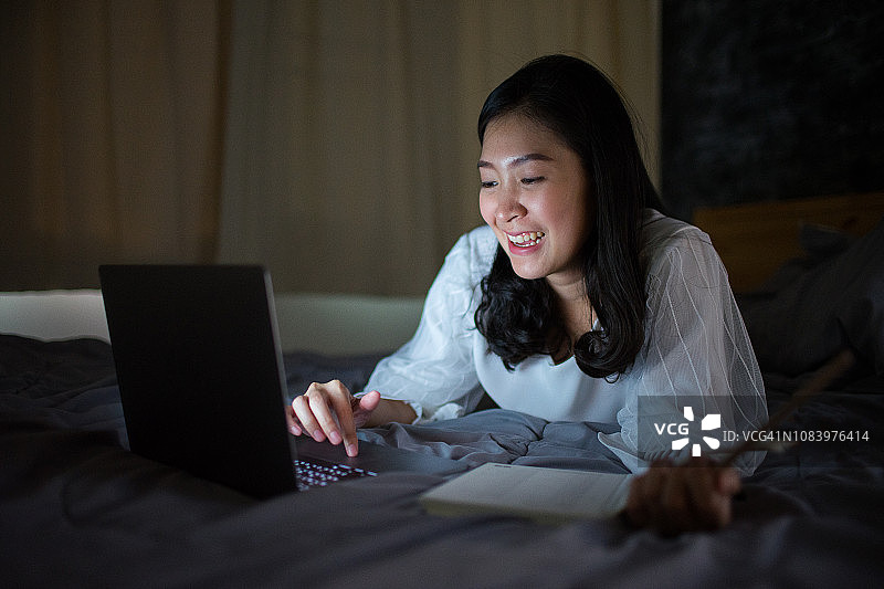 快乐的亚洲女性在床上用笔记本电脑从事在线业务图片素材