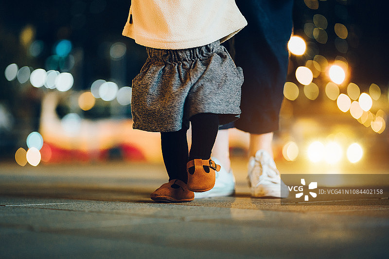 夜晚，母亲帮助女儿在城市街道灯光下迈出人生的第一步图片素材