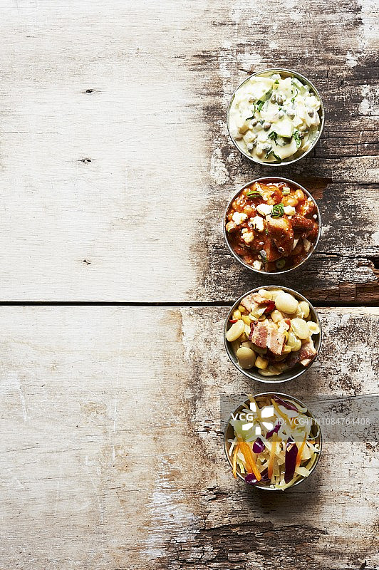 木桌上的小碗烧烤配菜：猪肉和豆类、土豆沙拉、凉拌卷心菜和杂烩图片素材