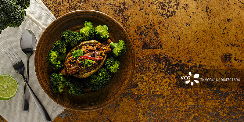 超级食物素食辣椒健康餐，由多种豆类和豆荚制成，搭配烤土豆和新鲜蒸西兰花，撒上酸橙汁，置于赤陶背景上图片素材