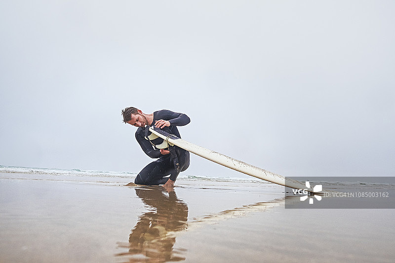 在康沃尔郡纽基的 Fistral 海滩秋季冲浪后，男子系上冲浪板系绳图片素材