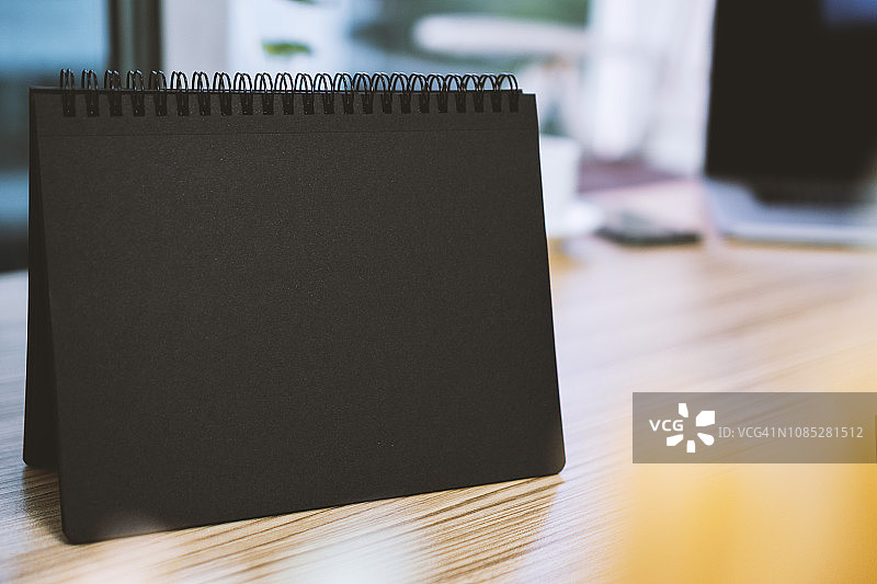 家庭办公室木桌上的空白黑色螺旋书图片素材