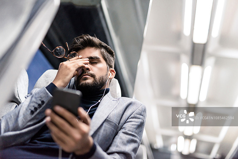 疲惫的年轻男人在火车上听播客时头痛图片素材