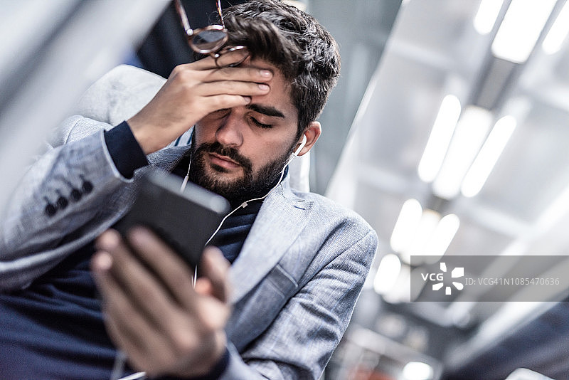疲惫的年轻男人在火车上听播客时头痛图片素材