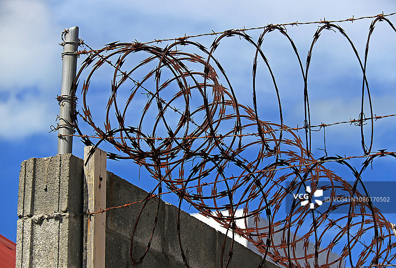 蓝色天空下混凝土围栏上的锈蚀带刺铁丝网图片素材