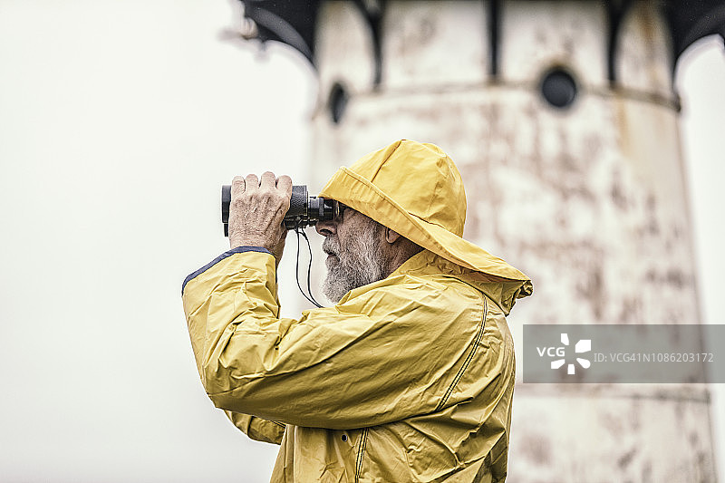 在灯塔附近用双筒望远镜观察的船长图片素材
