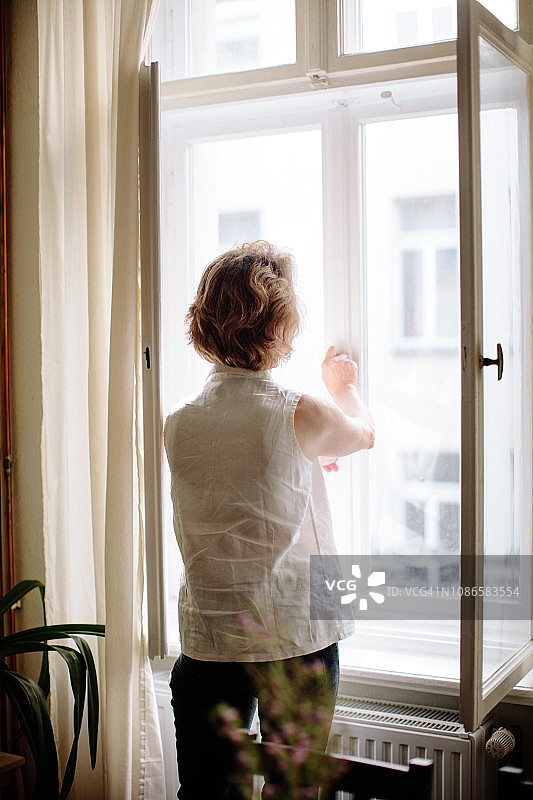 后视图年长妇女打开窗户在家里图片素材