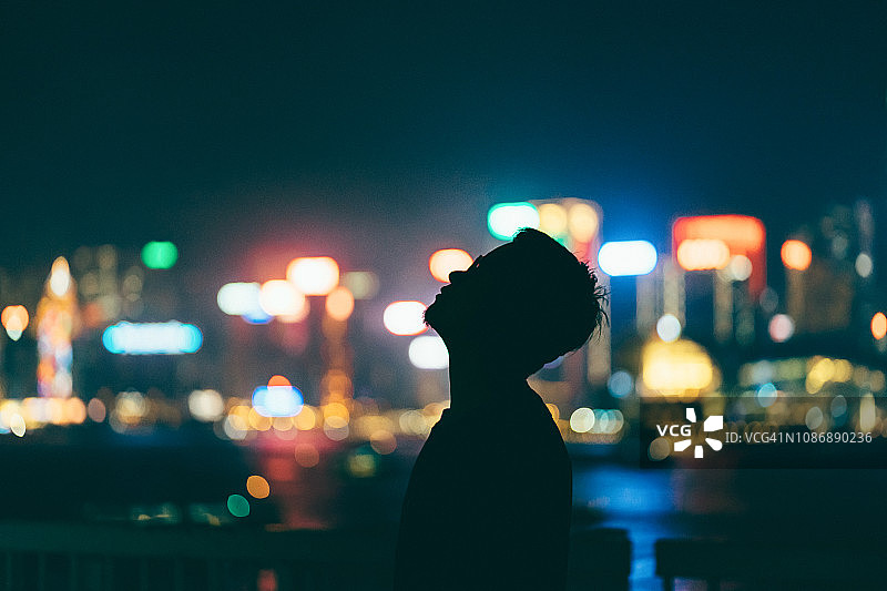 夜晚，在灯光璀璨、色彩缤纷的城市景观前，放松并仰望天空的男子轮廓图片素材