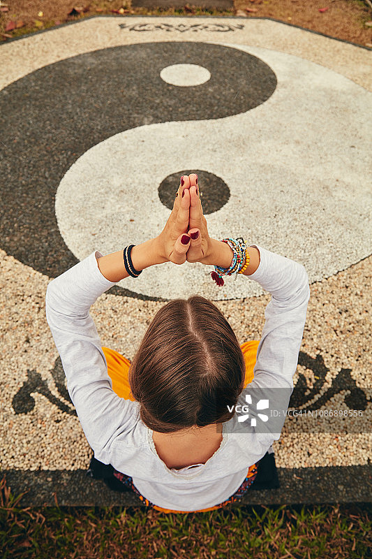年轻女人在带有阴阳标志的热带花园中练习瑜伽冥想图片素材
