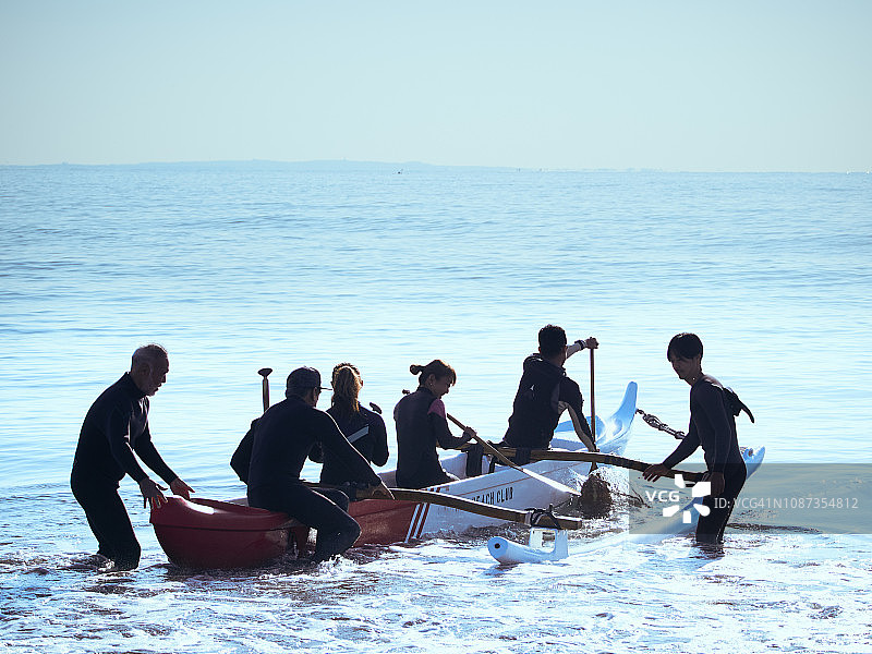 六名男女冲浪者在海浪边扛着可爱的独木舟图片素材