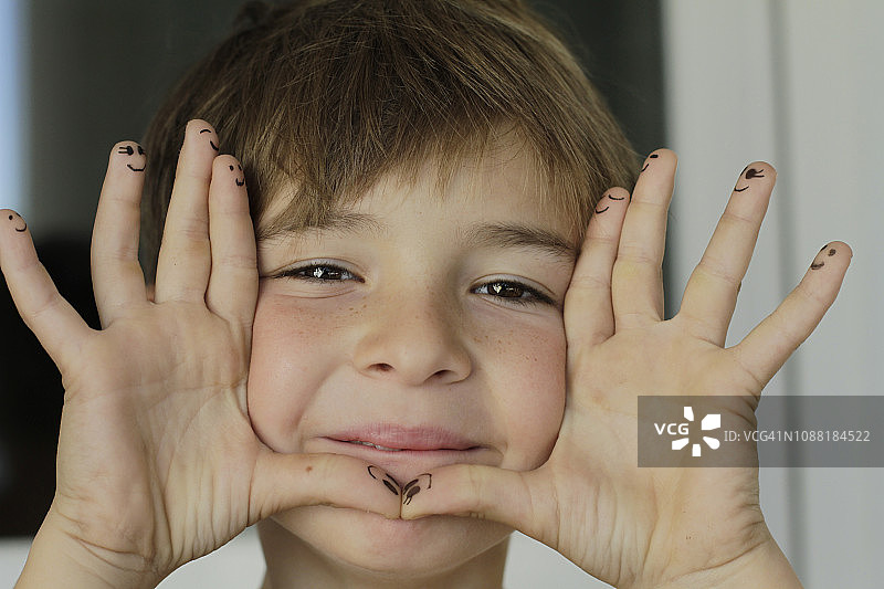 男孩展示手指上绘制的人脸图片素材