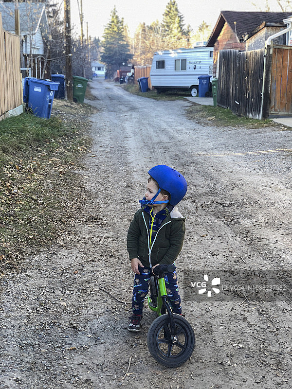 戴着蓝色头盔，坐在城市砾石路上的绿色自行车上的男孩图片素材