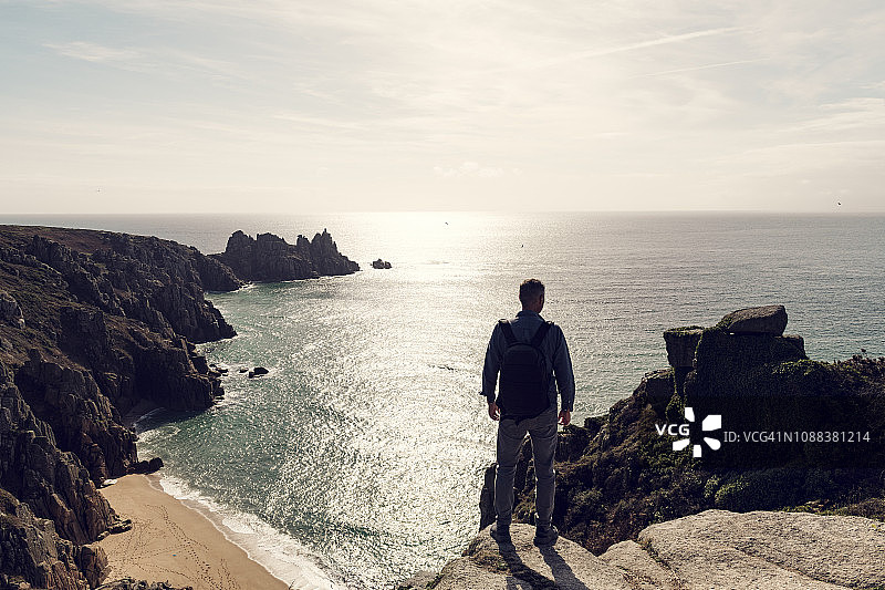 男人背着背包站在佩恩弗德海滩上，沐浴在秋日阳光中，南康沃尔，九月末图片素材