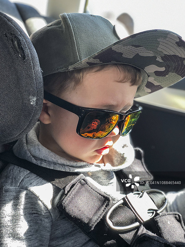 戴着成人帽子和太阳镜坐在汽车座椅上的小男孩图片素材