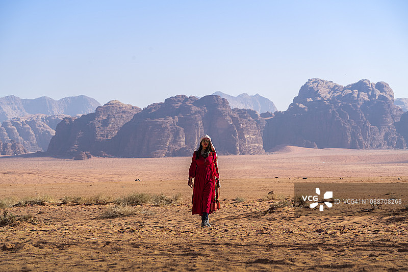 身穿红色连衣裙的女孩独自走在约旦瓦迪拉姆沙漠中图片素材