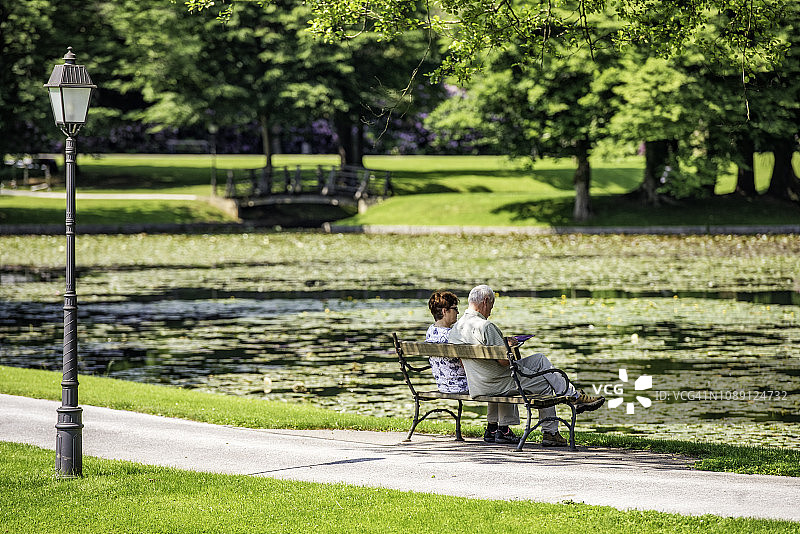 老年夫妇坐在公园湖边的长椅上图片素材