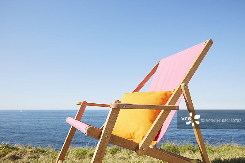 海边草地上带枕头的粉色沙滩椅，蓝色天空背景图片素材