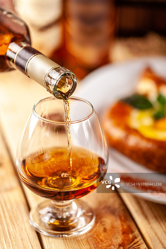 格鲁吉亚餐厅的概念。一个女孩把格鲁吉亚的白兰地从瓶子里倒进玻璃杯里。木桌上放着八叉藤图片素材