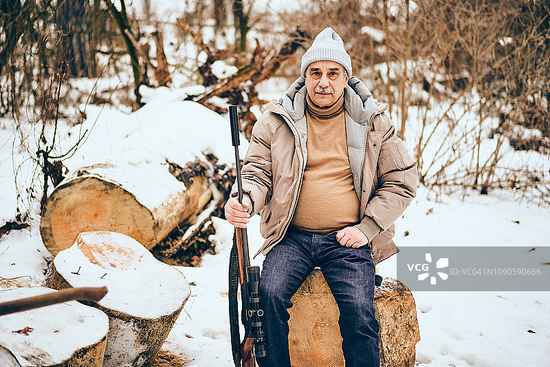 年长的男人坐在个人的木材场里，带着步枪图片素材