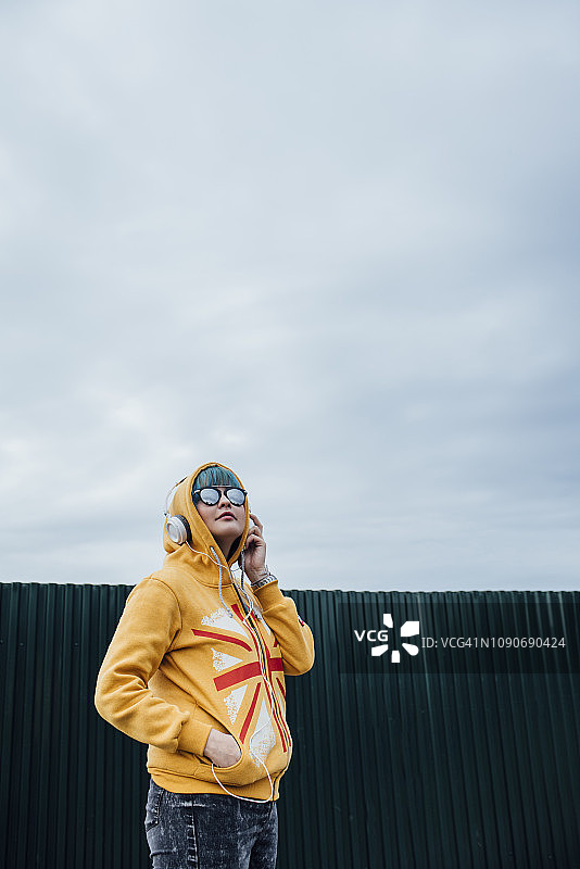 戴着耳机、穿着时尚连帽夹克的蓝色染发年轻女子肖像图片素材