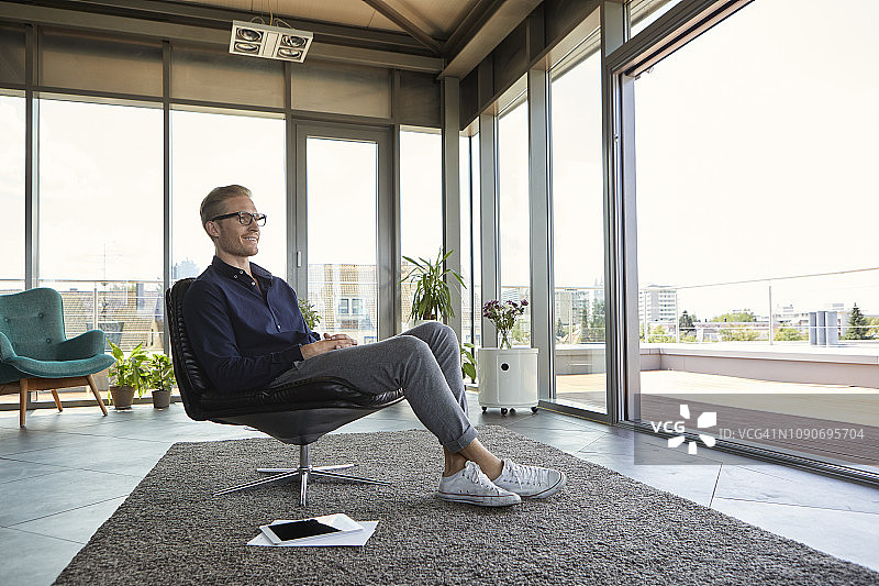 微笑的年轻男人坐在家中的窗边扶手椅上图片素材