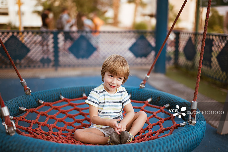 可爱的小男孩在游乐场的圆形秋千上放松图片素材