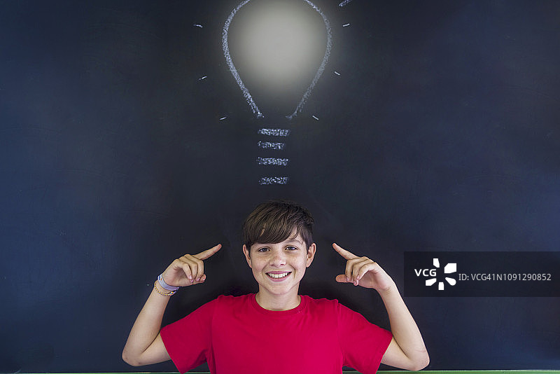 在教室里站在黑板上画灯泡的微笑男学生肖像图片素材