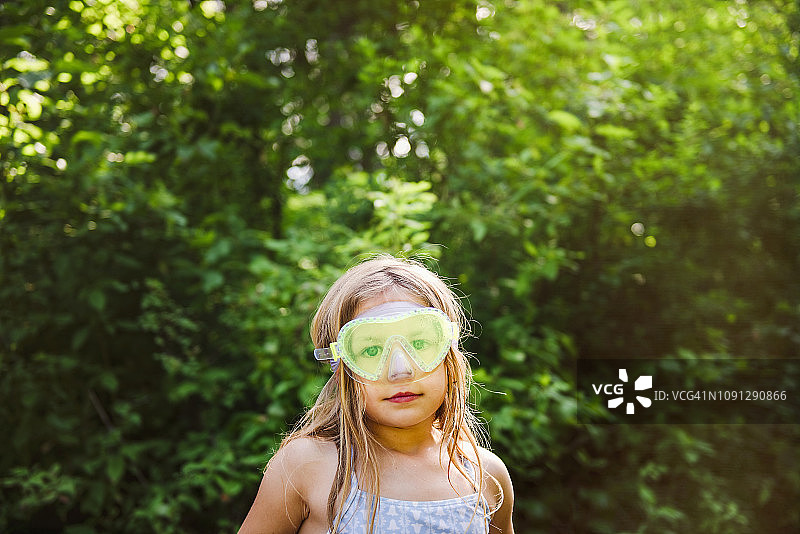 可爱的女孩戴着游泳镜站在森林的树旁图片素材