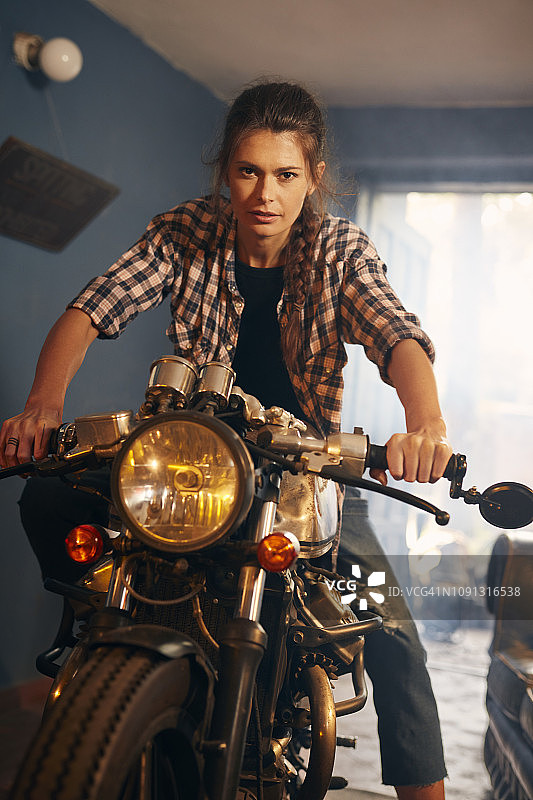 在摩托车修理店的女人，享受着她的定制摩托车图片素材