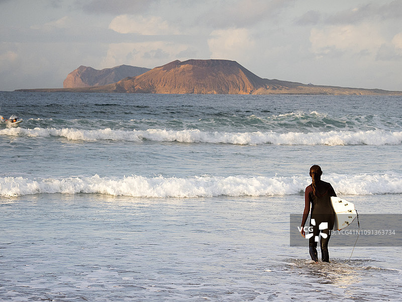 日落时分在西班牙加那利群岛兰萨罗特岛海滩上玩帆板的女人图片素材