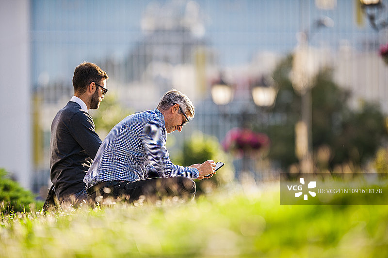 在城市里和同事一起使用手机的微笑男士图片素材