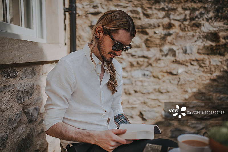 阳光明媚的日子里，英俊的年轻男人在户外阅读图片素材
