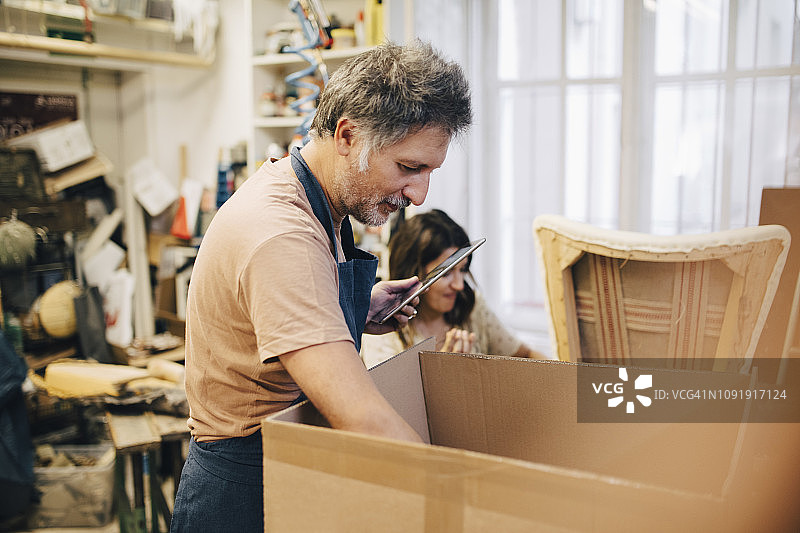 在工坊里拿着平板电脑看纸箱的男性工匠图片素材